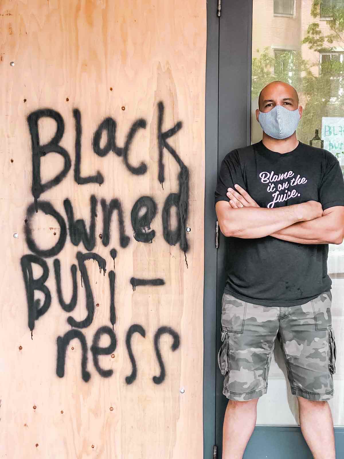 TJ Douglas standing beside a piece of plywood spray-painted with 'Black Owned Business'.