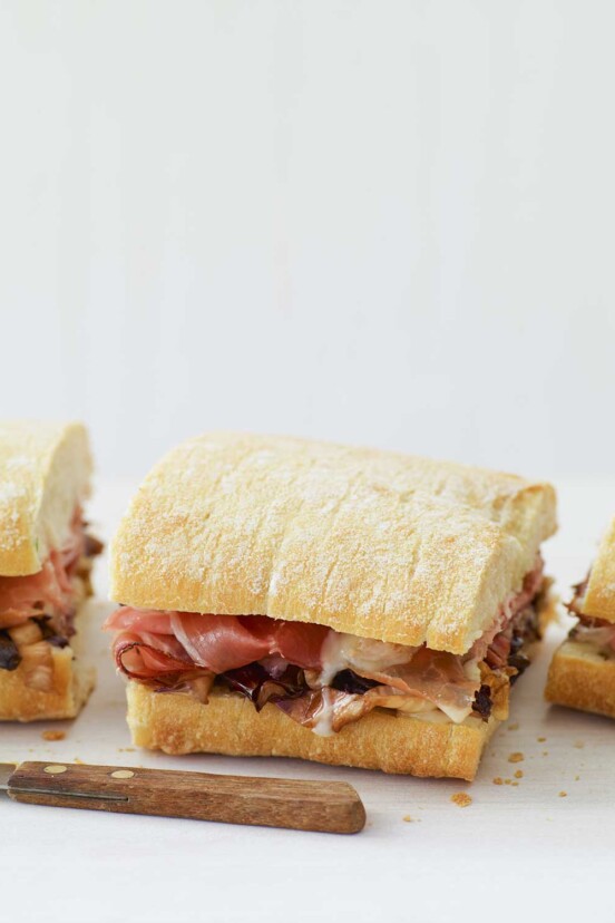 A warm panini with taleggio, grilled radicchio, and speck sandwich cut into thirds with a knife in front of the sandwich.