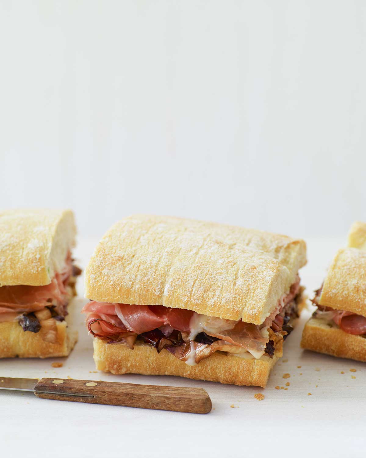 En varm panini med taleggio, grillad radicchio och fläckmacka skuren i tredjedelar med en kniv framför smörgåsen.