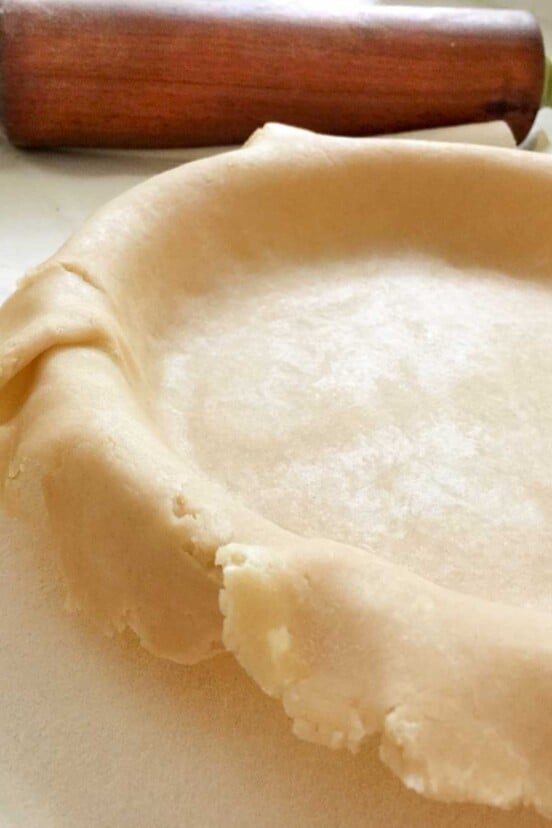 An all-butter pie crust laying in a pie pan with a rolling pin beside it.