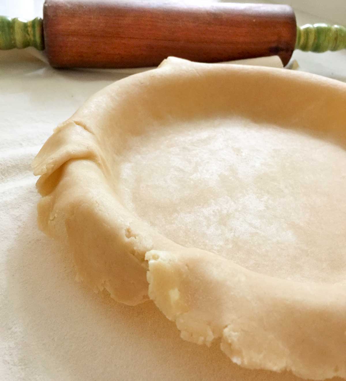 An all-butter pie crust laying in a pie pan with a rolling pin beside it.