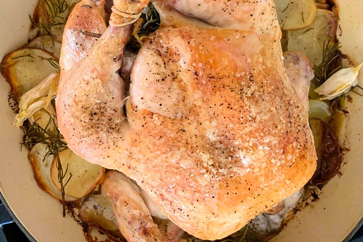 A whole roast chicken with rosemary and potatoes.