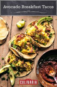 Three avocado breakfast tacos with eggs, bacon, shallots, and chives with a bowl of salsa on the side.