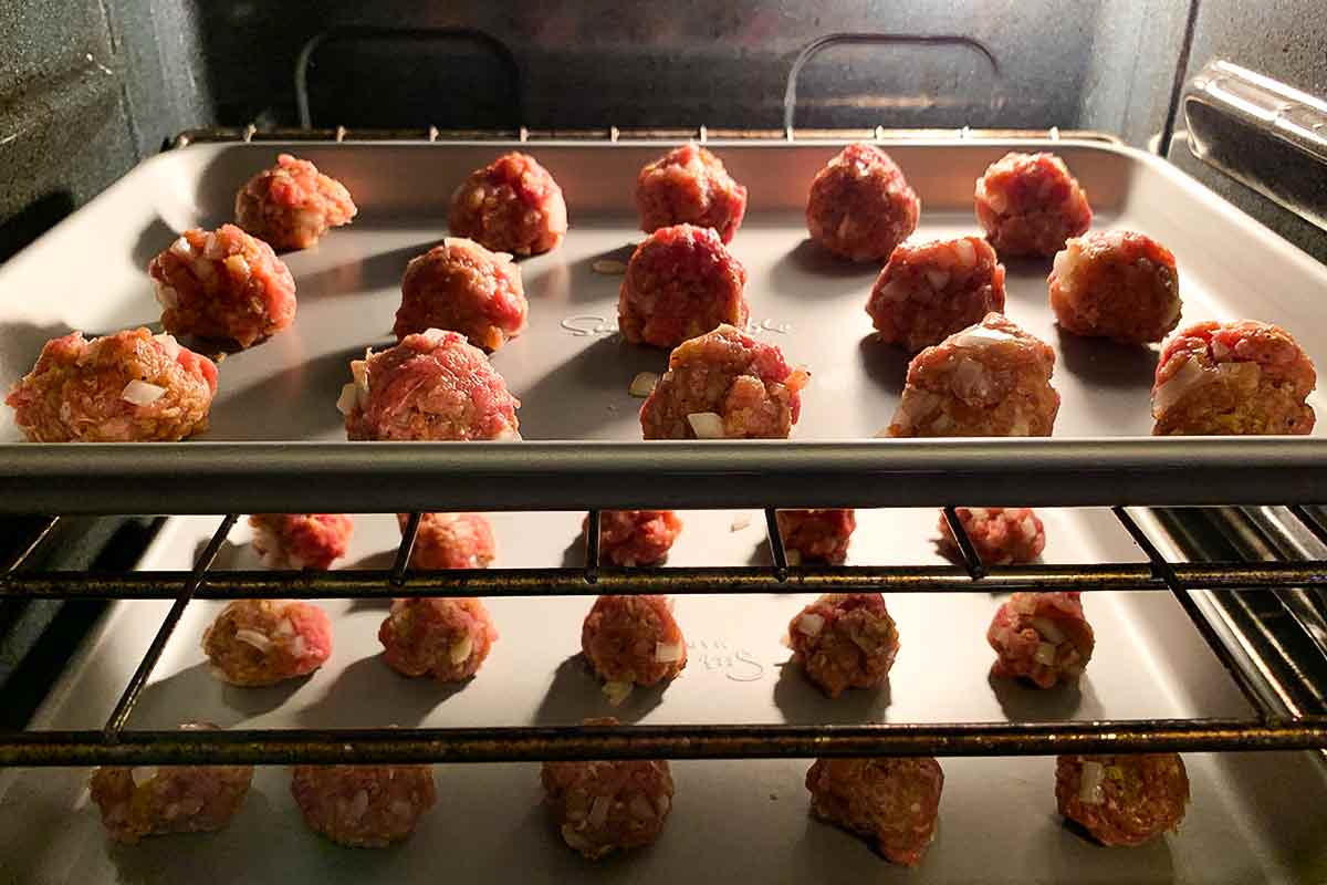 Two trays of unbaked bbq meatballs in the oven.
