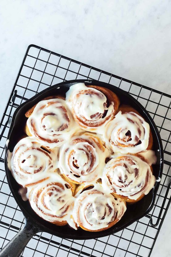 A cast-iron skillet filled with glazed biscuit cinnamon rolls on a wire rack.