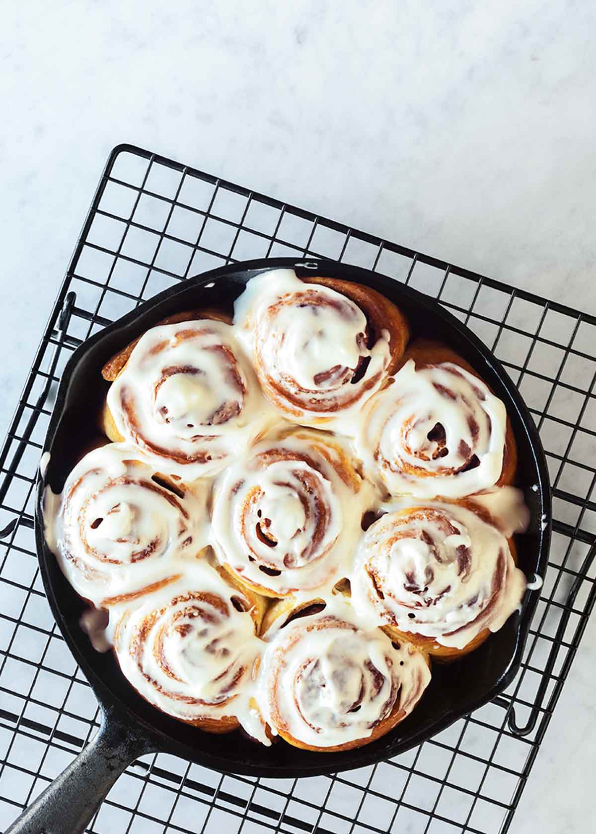 A cast iron skillet filled with glazed biscuit cinnamon rolls on a wire rack.