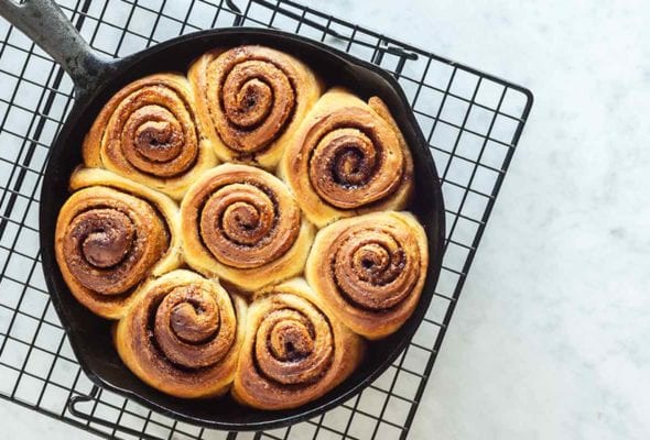A cast-iron skillet filled with unglazed biscuit cinnamon rolls on a wire rack.