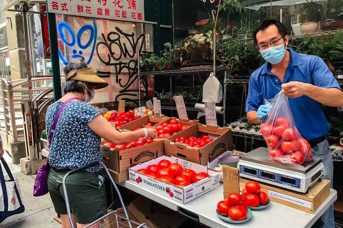 An Asian man with a mask bagging tomatoes and a woman shopping for tomatoes for the podcast Ep. 31: Grace Young: Coronavirus: Chinatown Stories.