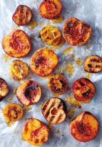 Grilled peaches with honey and black pepper scattered on a piece of parchment paper.