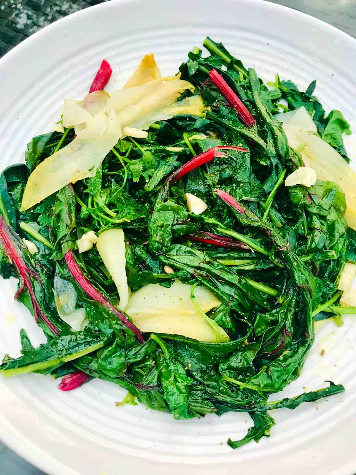 A white plate filled with horta, or boiled greens with garlic.
