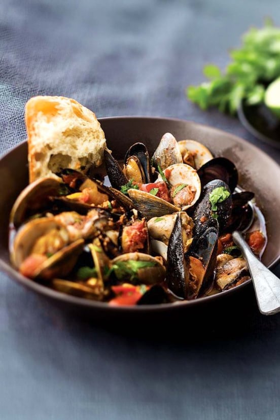 A black bowl of cod, mussels, clams, and shrimp with bread.