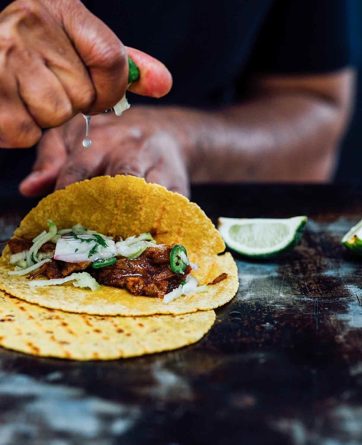 A person squeezing lime juice over an open pulled pork taco.