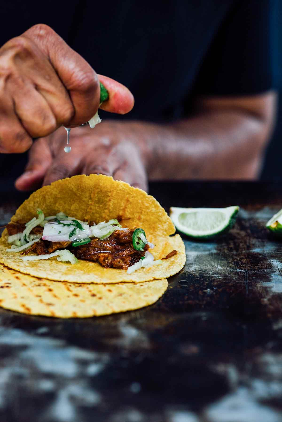 A person squeezing lime juice over an open pulled pork taco.