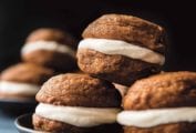 Two plates each with four pumpkin spice whoopie pies with cream cheese filling stacked on them.