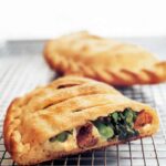 Two ricotta calzones with sausage and broccoli rabe, one cut in half, the other whole, on a wire rack
