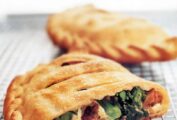 Two ricotta calzones with sausage and broccoli rabe, one cut in half, the other whole, on a wire rack