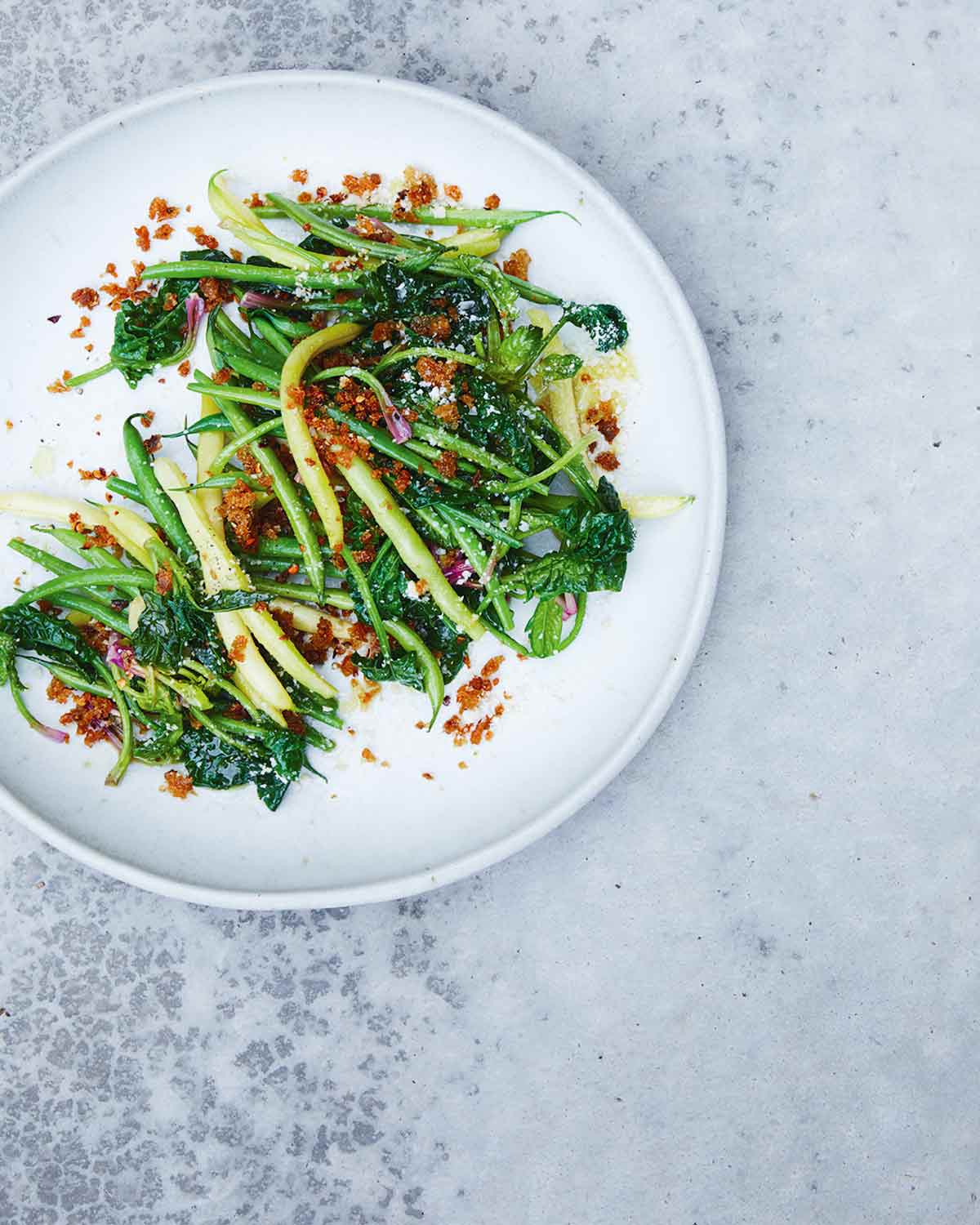 A round white plate topped with sautéed green beans and spinach with bread crumbs sprinkled over the top.