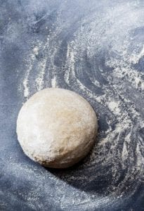 A ball of semolina pizza dough on a floured surface.