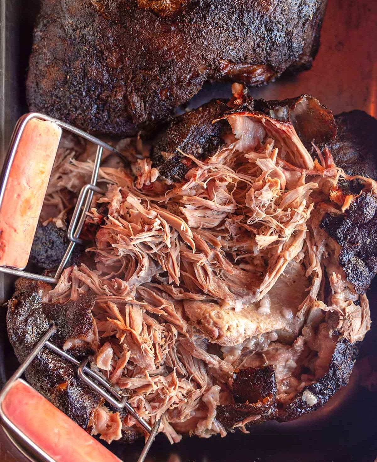 Cheap Cuts: Partially shredded slow cooker pulled pork with two large forks shredding it.