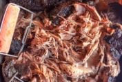 Partially shredded slow cooker pulled pork with two large forks shredding it.