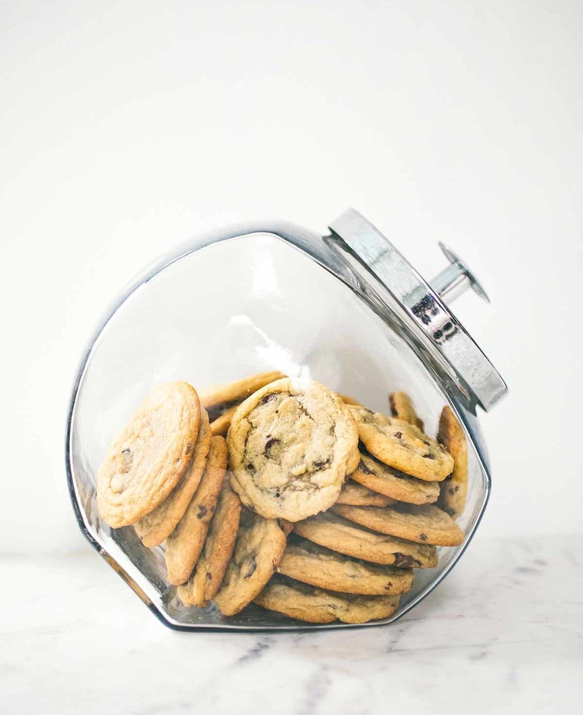A glass jar filled with soft chocolate chip cookies.