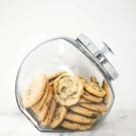 A glass jar filled with soft chocolate chip cookies.