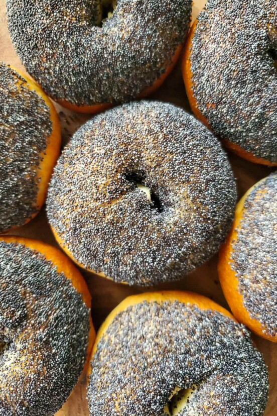 Seven sourdough bagels topped with poppy seeds.