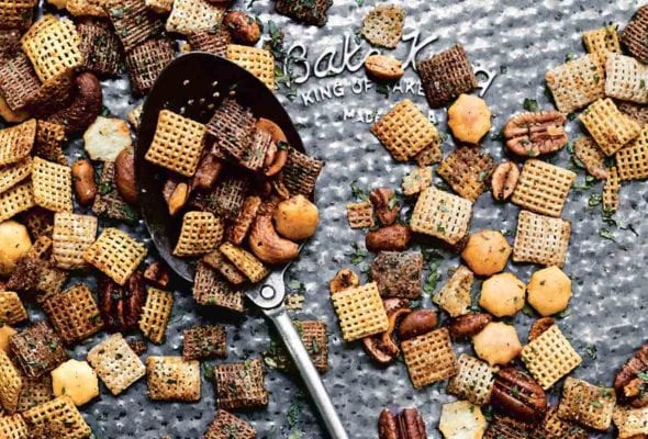 Spicy Chex mix scattered on a baking sheet with a spoon lying in the middle.