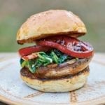 A spinach tomato mushroom burger between two toasted bun halves on a brown plate.