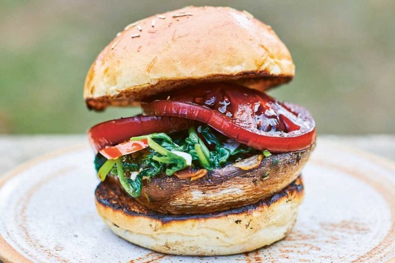 A spinach tomato mushroom burger between two toasted bun halves on a brown plate.