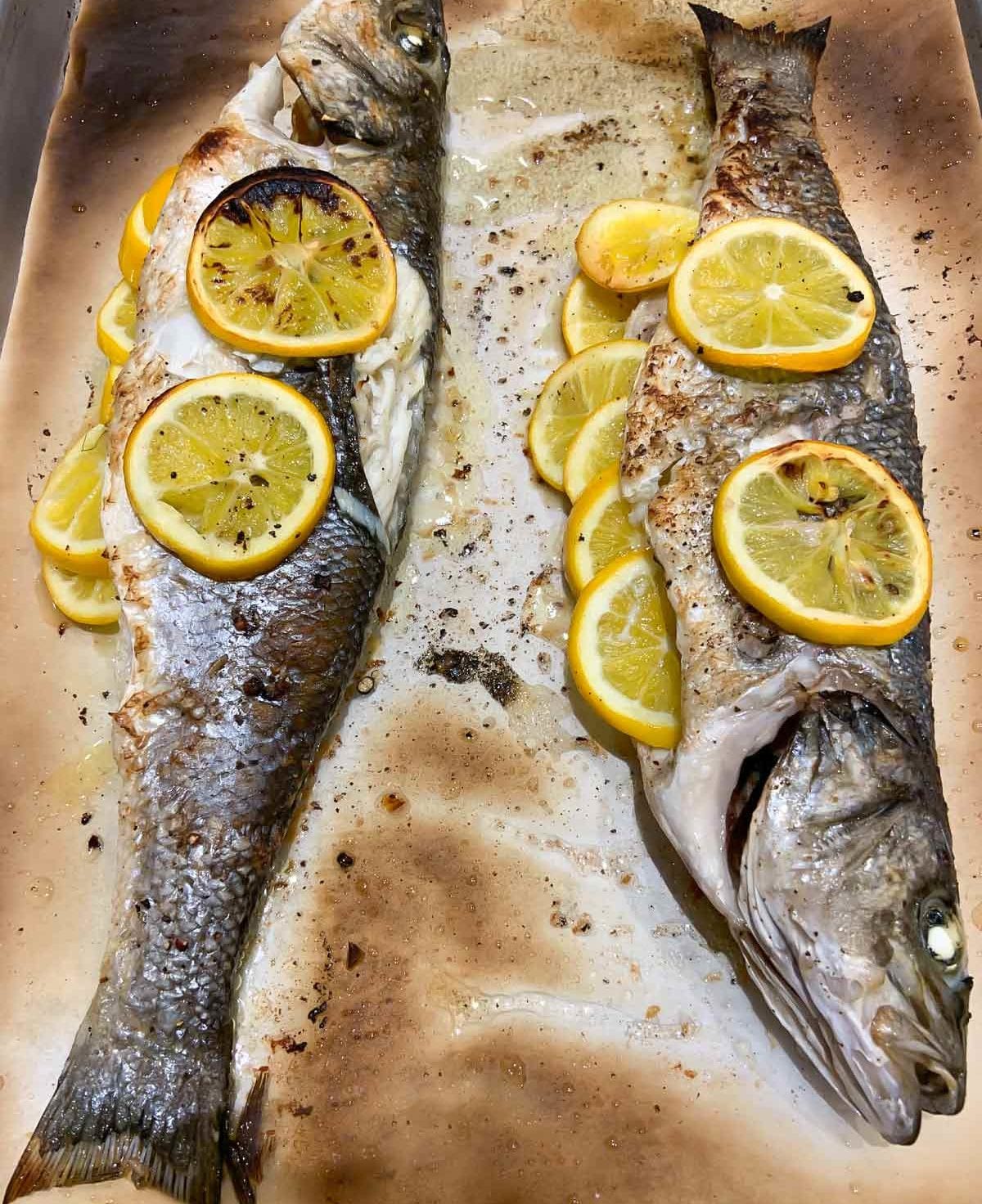 Two whole roasted branzino with lemon and shaved fennel salad on a parchment-lined baking sheet.