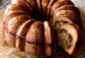 An apple coffee cake with one slice cut from it on a wire cooling rack with parchment underneath.