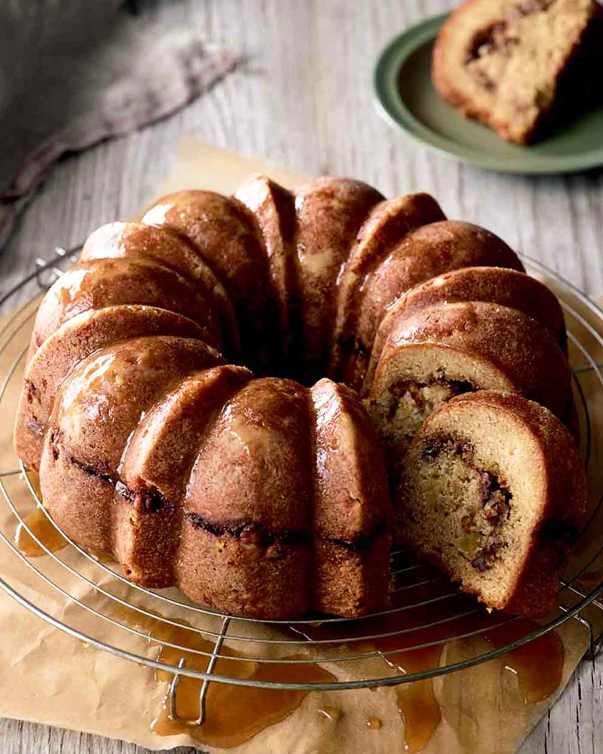 An apple coffee cake with one slice cut from it on a wire cooling rack with parchment underneath.