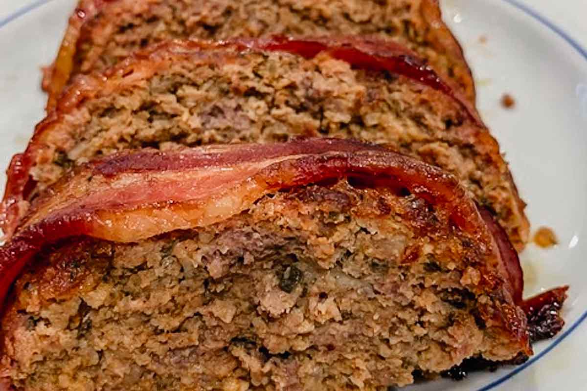 A sliced bacon-wrapped meatloaf on a white platter.