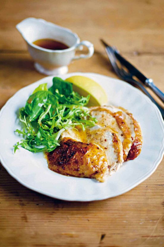 Slices of baked chicken drizzled with cinnamon butter, green salad, and lemon wedge.