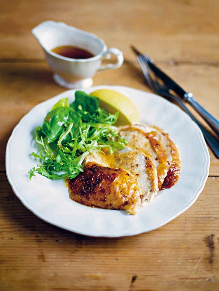 Slices of baked chicken drizzled with cinnamon butter, green salad, and lemon wedge.