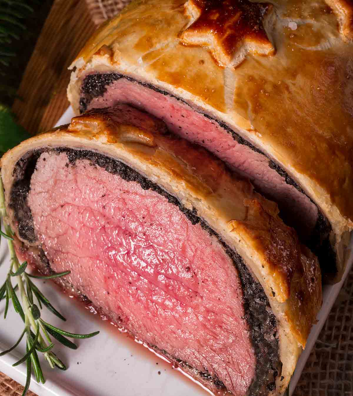 Close-up of a beef Wellington on a plate with a sprig of rosemary