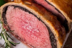 Close-up of a beef Wellington on a plate with a sprig of rosemary