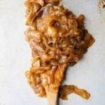 A scoop of big batch caramelized onions on a wooden spoon.