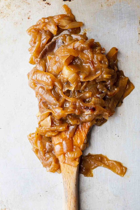 A scoop of big batch caramelized onions on a wooden spoon.