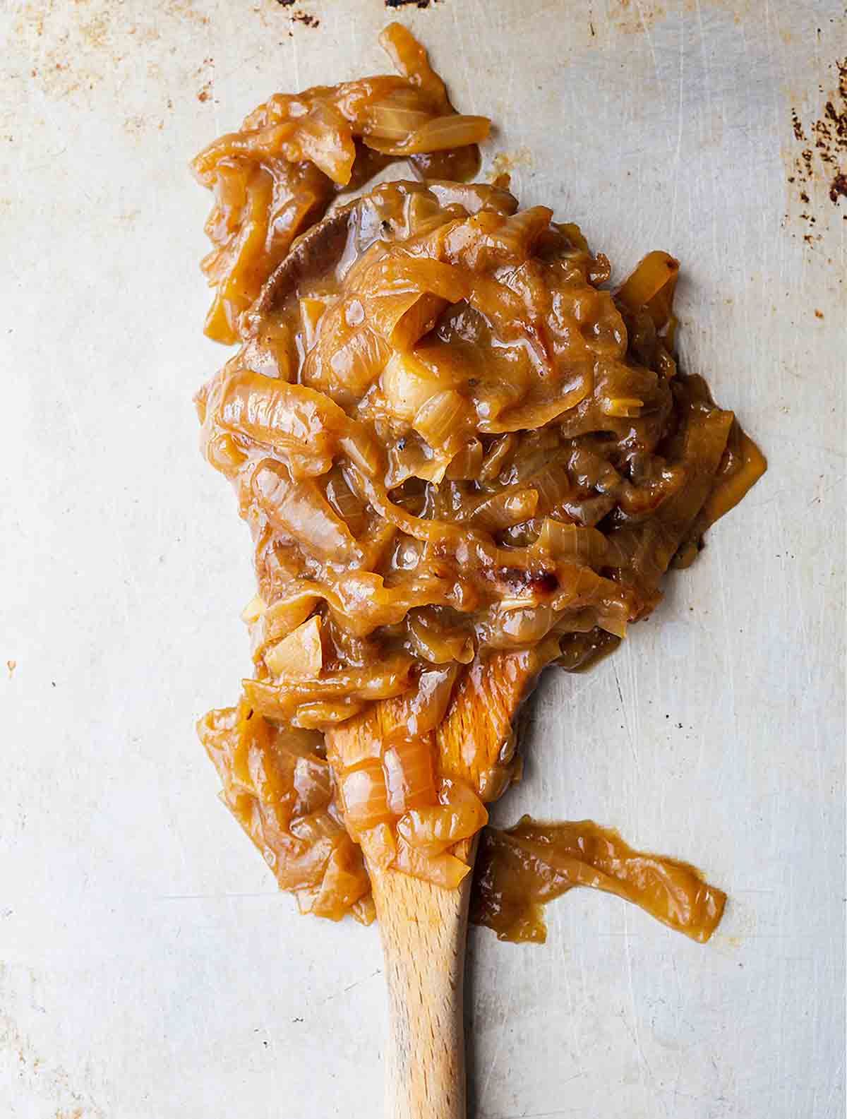 A scoop of big batch caramelized onions on a wooden spoon.