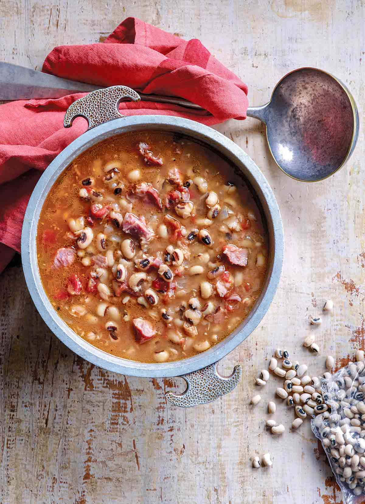 Bowl of black-eyed peas in a tomato broth on a sheet of wood.