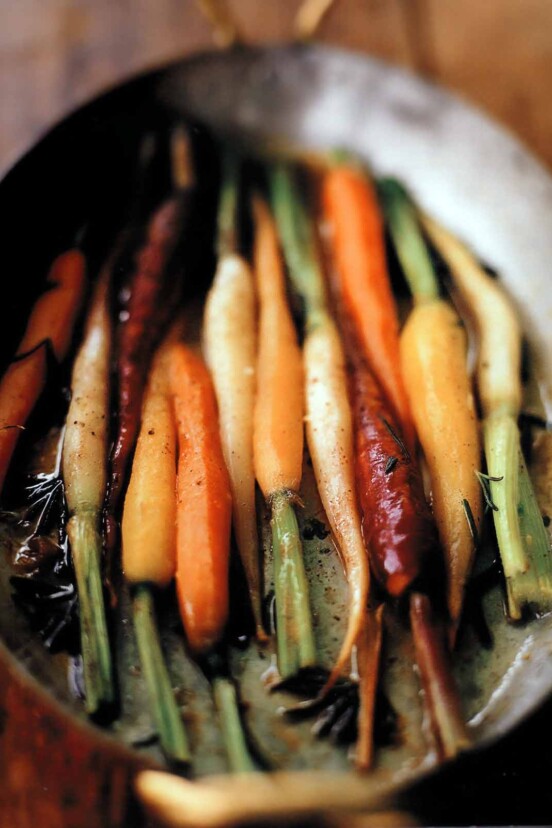 Assorted colors of braised carrots with orange and rosemary in a dish.