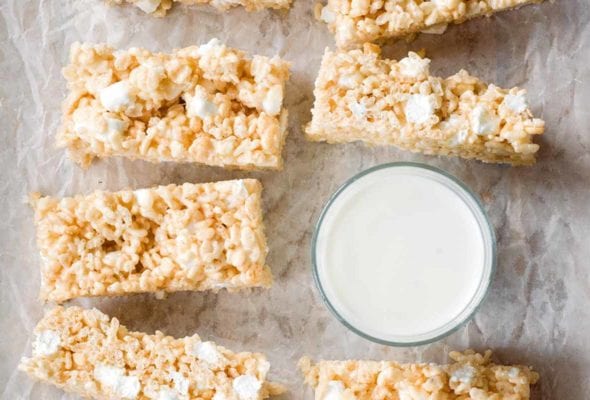 Nine brown butter rice krispies treats next to a glass of milk.