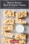 Nine brown butter rice krispies treats next to a glass of milk.