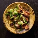 A wooden bowl filled with roasted Brussels sprouts with guanciale.