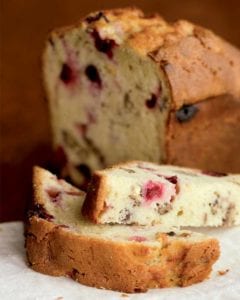 A loaf of cranberry orange pecan bread in the background with a halved slice from it in front
