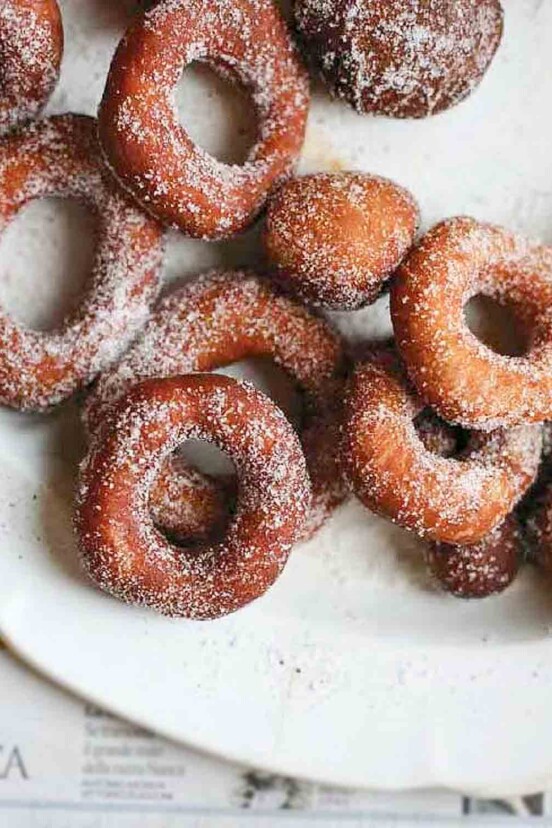 A pile of sugar-dusted easy raised doughnuts on a white plate.