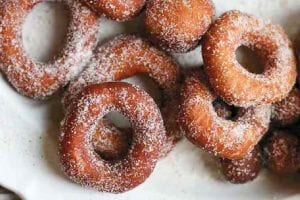 A pile of sugar-dusted easy raised doughnuts on a white plate.