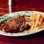 A green and white patterned plate filled with entrecôte à l'anchoïade and a pile of French fries